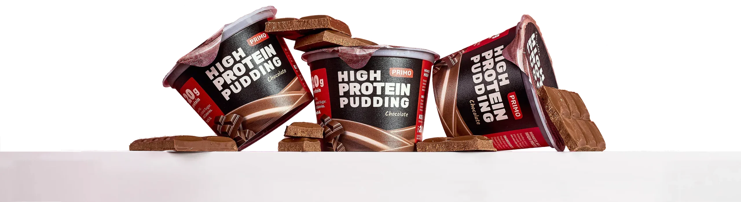 Three cups of Primo Chocolate High Protein Pudding surrounded by chunks of chocolate, arranged against a clean white background.